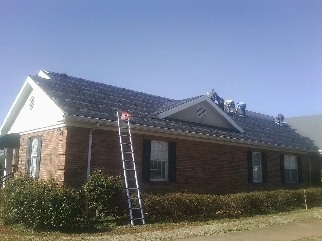 Crew tearing shingles off a brick ranch roof with a ladder set — Emergency Roof Repair work by our crew in Granger