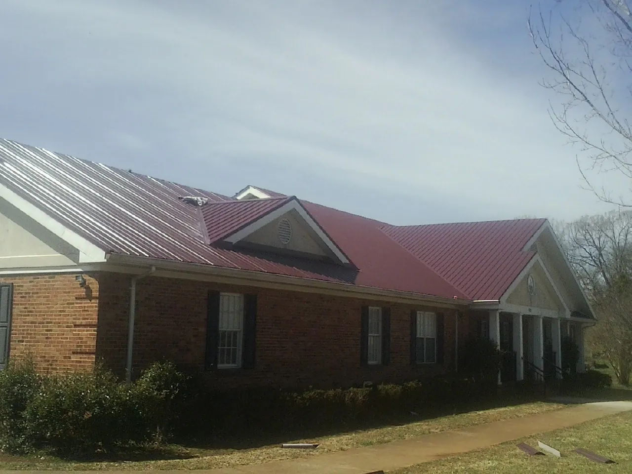 Red metal roof with gabled entries on a long brick building, from a Hail Damage Roof Repair job in Granger