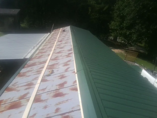 Old rusted panels beside newly installed green metal roofing — Wind Damage Roof Repair by Roofing Brothers in Granger